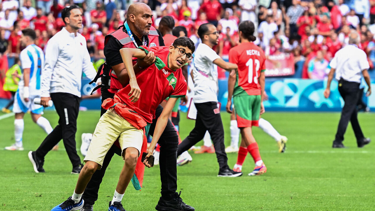 TOPSHOT - A member of security holds a fan of Morocco after numerous Morocco's fans invaded the pitch at the end of the men's group B football match between Argentina and Morocco during the Paris 2024 Olympic Games at the Geoffroy-Guichard Stadium in Saint-Etienne on July 24, 2024.
