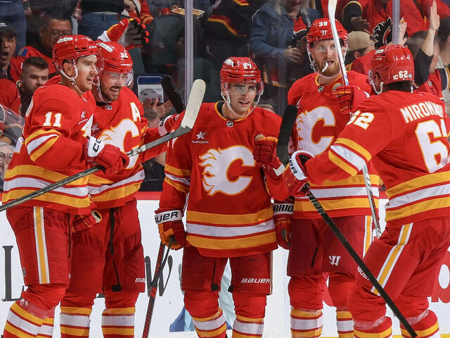 CALGARY, AB - OCTOBER 15: Matt Coronato #27 of the Calgary Flames celebrates with teammates Daniil Miromanov #62, Mikael Backlund #11 after a goal against PLAYER of the Chicago Blackhawks at Scotiabank Saddledome on October 15, 2024 in Calgary, Alberta, Canada.
