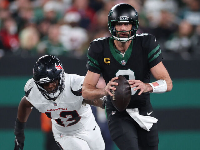 EAST RUTHERFORD, NEW JERSEY - OCTOBER 31: Aaron Rodgers #8 of the New York Jets is tackled by Neville Hewitt #43 of the Houston Texans during the third quarter at MetLife Stadium on October 31, 2024 in East Rutherford, New Jersey.