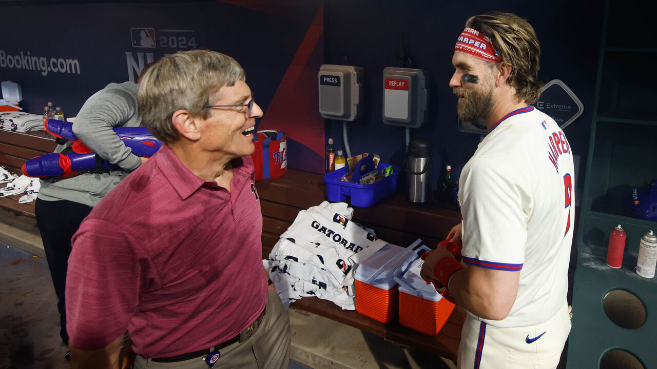 PHILADELPHIA, PA - OCTOBER 06: Bryce Harper #3 of the Philadelphia Phillies talks with team owner John Middleton in the dugout after winning Game 2 of the Division Series presented by Booking.com between the New York Mets and the Philadelphia Phillies at Citizens Bank Park on Sunday, October 6, 2024 in Philadelphia, Pennsylvania.