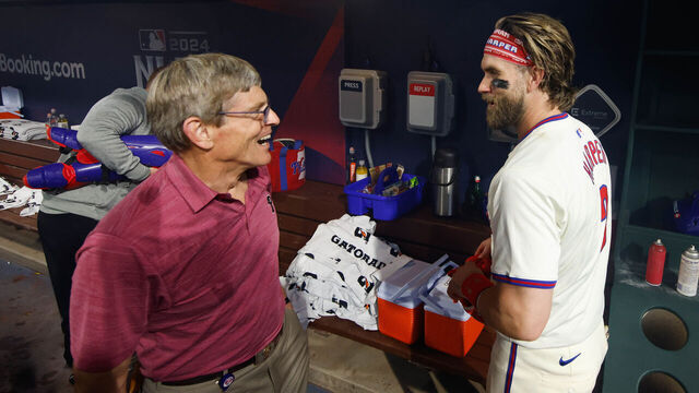 PHILADELPHIA, PA - OCTOBER 06: Bryce Harper #3 of the Philadelphia Phillies talks with team owner John Middleton in the dugout after winning Game 2 of the Division Series presented by Booking.com between the New York Mets and the Philadelphia Phillies at Citizens Bank Park on Sunday, October 6, 2024 in Philadelphia, Pennsylvania.