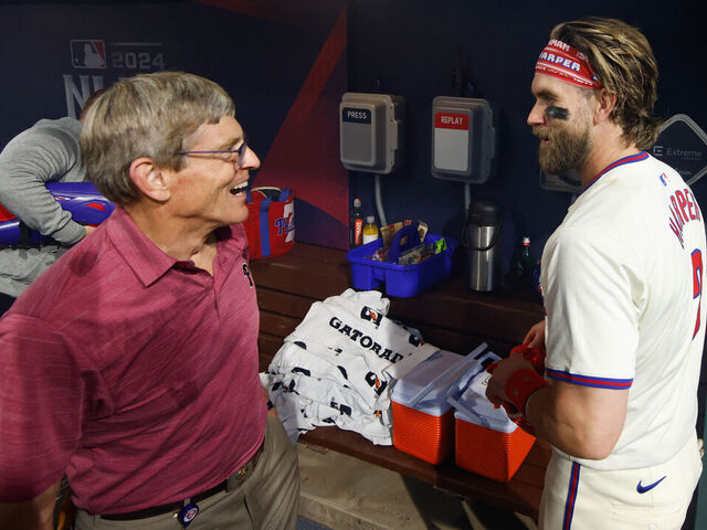 PHILADELPHIA, PA - OCTOBER 06: Bryce Harper #3 of the Philadelphia Phillies talks with team owner John Middleton in the dugout after winning Game 2 of the Division Series presented by Booking.com between the New York Mets and the Philadelphia Phillies at Citizens Bank Park on Sunday, October 6, 2024 in Philadelphia, Pennsylvania.