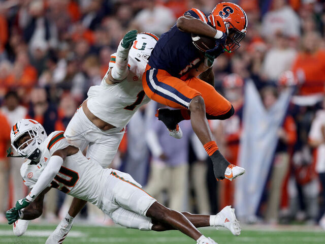 SYRACUSE, NEW YORK - NOVEMBER 30: OJ Frederique Jr. #29 and Francisco Mauigoa #1 of the Miami Hurricanes attempt to tackle LeQuint Allen #1 of the Syracuse Orange as he leaps over them during the third quarter at JMA Wireless Dome on November 30, 2024 in Syracuse, New York.