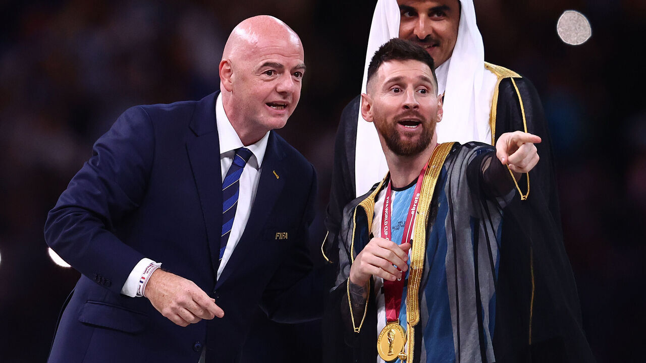 LUSAIL CITY, QATAR - DECEMBER 18: Lionel Messi of Argentina gestures before receiving the FIFA World Cup trophy from FIFA President Gianni Infantino as Sheikh Tamim bin Hamad Al Thani, Emir of Qatar looks on during the FIFA World Cup Qatar 2022 Final match between Argentina and France at Lusail Stadium on December 18, 2022 in Lusail City, Qatar.
