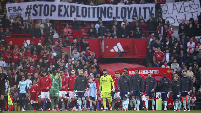 MANCHESTER, ENGLAND - MARCH 9: Players walk out under a fan banner in the crowd the Premier League match between Manchester United FC and Arsenal FC at Old Trafford on March 9, 2025 in Manchester, England.