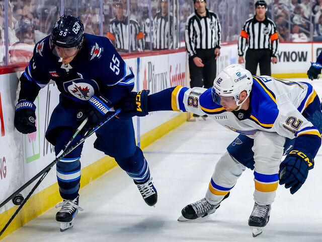 WINNIPEG, CANADA - APRIL 21: Mark Scheifele #55 of the Winnipeg Jets and Radek Faksa #12 of the St. Louis Blues chase the puck along the boards during second period action in Game Two of the First Round of the 2025 Stanley Cup Playoffs at Canada Life Centre on April 21, 2025 in Winnipeg, Manitoba, Canada.
