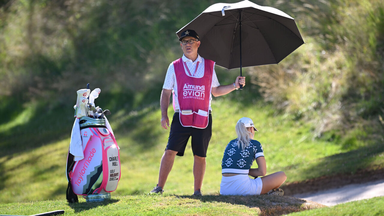 EVIAN-LES-BAINS, FRANCE - JULY 10: Caddie Adam Woodward holds a umbrella over Charley Hull of England as she sits in the shade on the third hole, before later withdrawing from play, during Round One of The Amundi Evian Championship 2025 at Evian Resort Golf Club on July 10, 2025 in Evian-les-Bains, France.