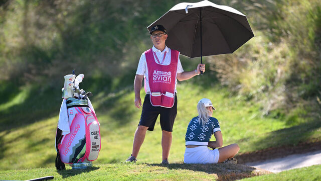 EVIAN-LES-BAINS, FRANCE - JULY 10: Caddie Adam Woodward holds a umbrella over Charley Hull of England as she sits in the shade on the third hole, before later withdrawing from play, during Round One of The Amundi Evian Championship 2025 at Evian Resort Golf Club on July 10, 2025 in Evian-les-Bains, France.