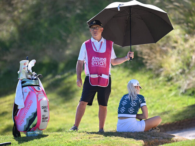 EVIAN-LES-BAINS, FRANCE - JULY 10: Caddie Adam Woodward holds a umbrella over Charley Hull of England as she sits in the shade on the third hole, before later withdrawing from play, during Round One of The Amundi Evian Championship 2025 at Evian Resort Golf Club on July 10, 2025 in Evian-les-Bains, France.