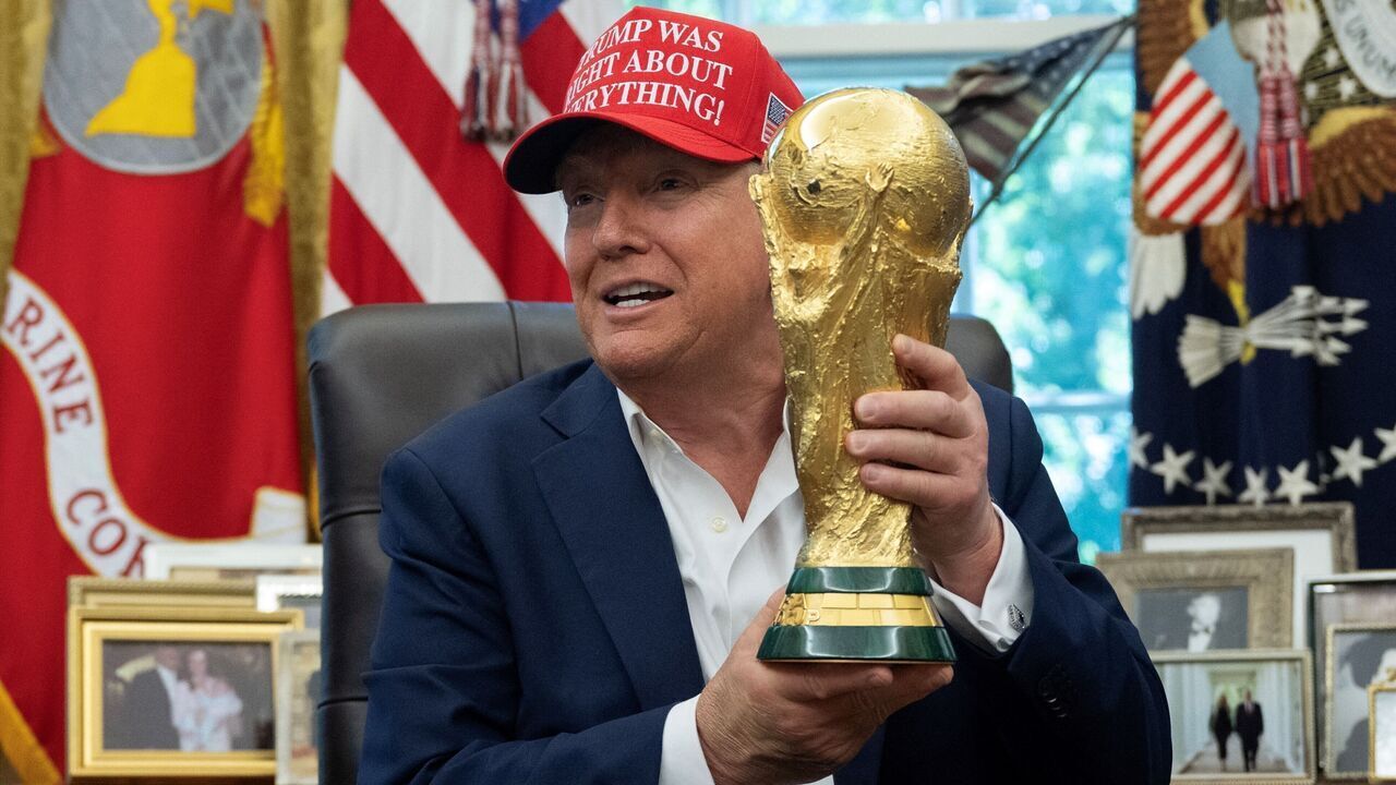 US President Donald Trump holds the World Cup trophy in the Oval Office of the White House in Washington, DC, on August 22, 2025. Trump announced the 2026 World Cup draw will be held on December 5 at Washington's Kennedy Center.