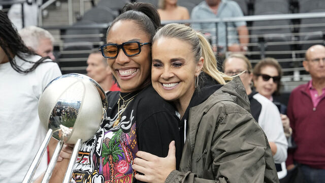 LAS VEGAS, NEVADA - OCTOBER 12: A'ja Wilson (L) #22 and head coach Becky Hammon of the Las Vegas Aces embrace with the 2025 WNBA championship trophy on the field before a game between Tennessee Titans and Las Vegas Raiders at Allegiant Stadium on October 12, 2025 in Las Vegas, Nevada.