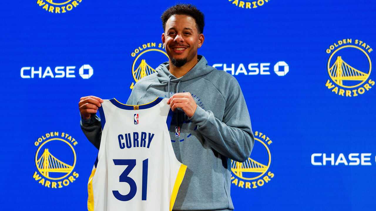 Golden State Warriors guard Seth Curry (31), the younger brother of Warriors guard Stephen Curry (30), holds his new jersey during a press conference following basketball practice at the Chase Center in San Francisco on Thursday, October 2, 2025.