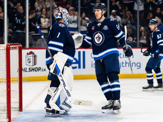 WINNIPEG, CANADA - DECEMBER 5: Eric Comrie #1 and Logan Stanley #64 of the Winnipeg Jets celebrate a 4-1 victory against the Buffalo Sabres at Canada Life Centre on December 5, 2025 in Winnipeg, Manitoba, Canada.