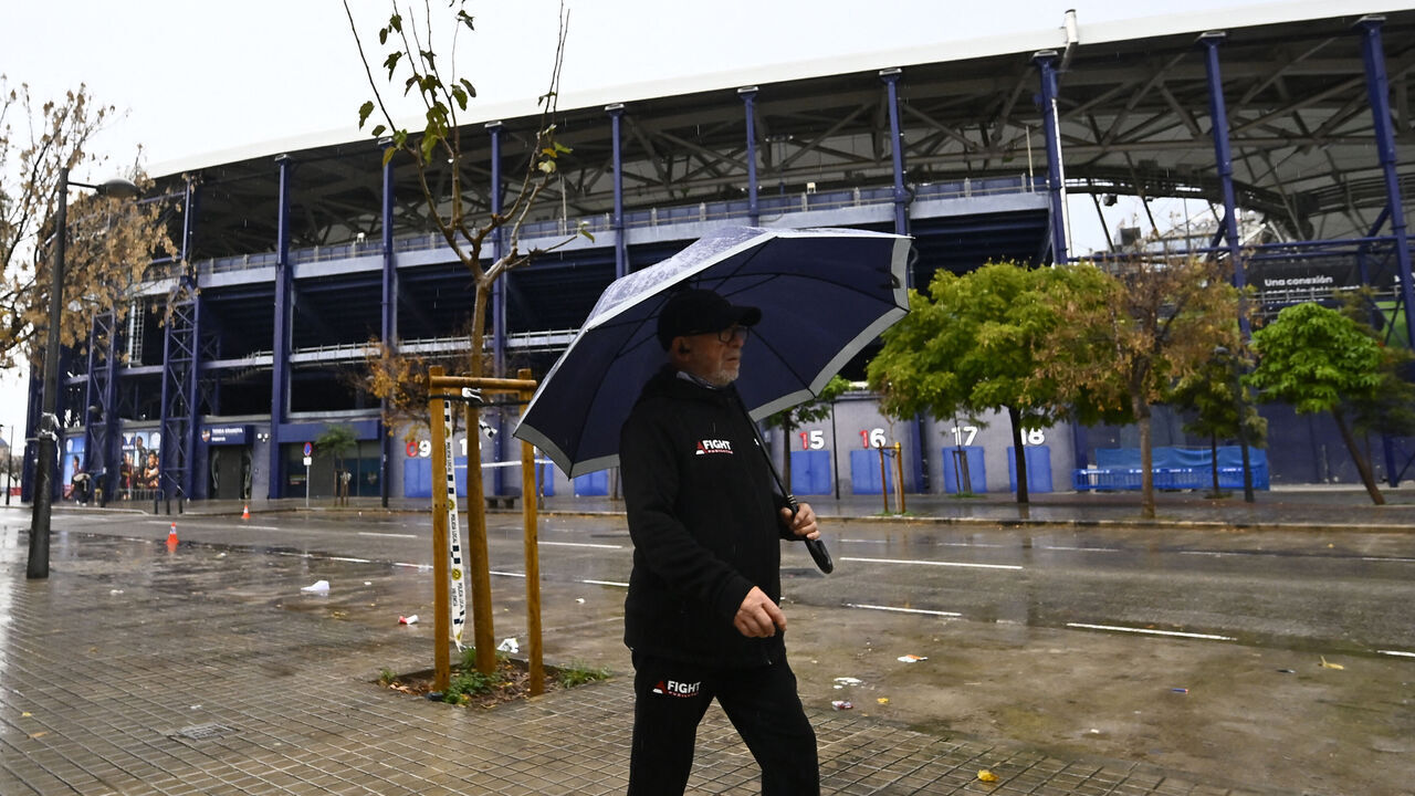 A man walks with an umbrella outside the Ciutat de Valencia stadium after the Spanish league football match between Levante UD and Villarreal CF was suspended due to severe weather warning of torrential rains in Valencia on December 14, 2025.