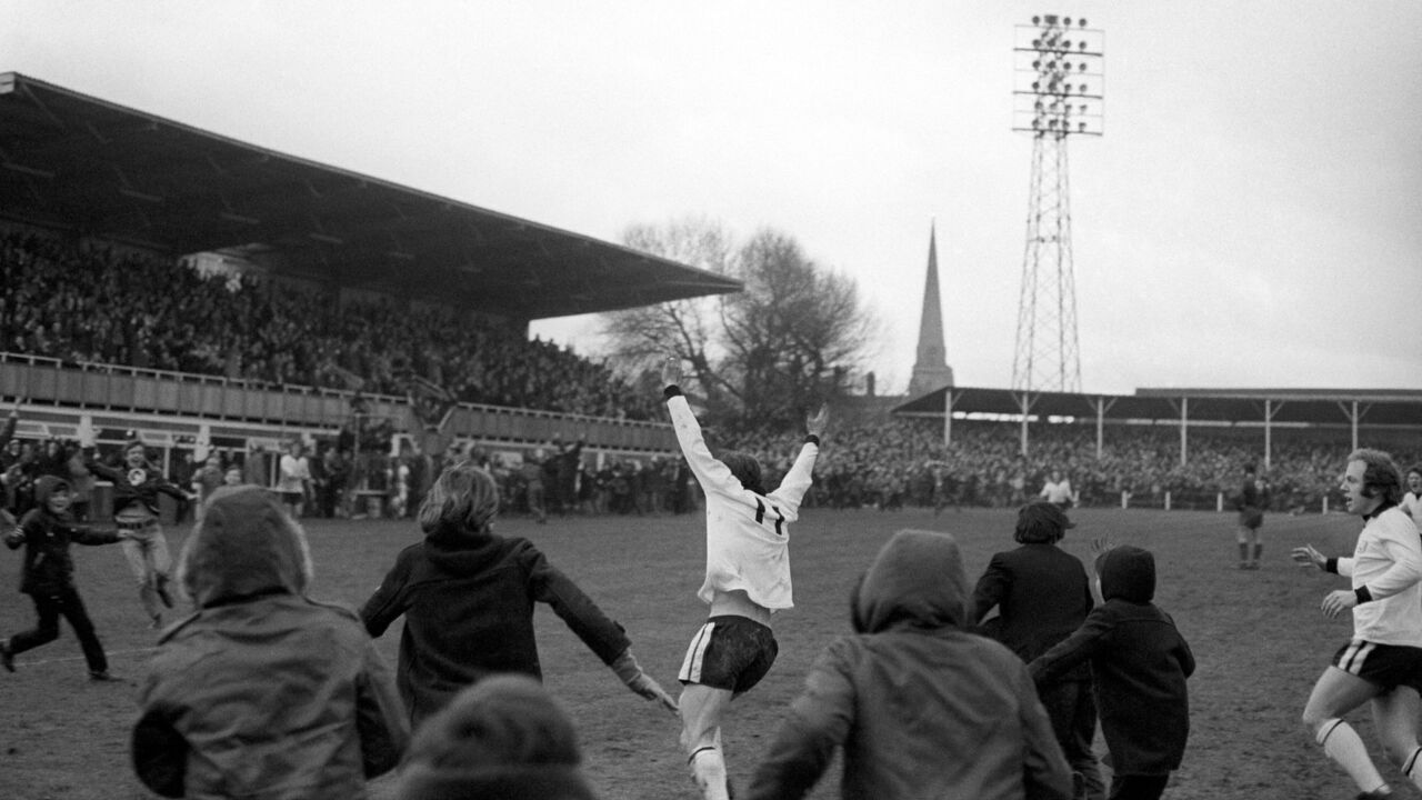 Hereford United's Ronnie Radford (c) is pursued by hundreds of young fans, and teammate Ricky George (r - scorer of the winning goal in extra time), after scoring the equalizing goal four minutes from time