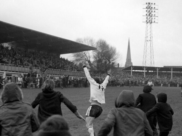 Hereford United's Ronnie Radford (c) is pursued by hundreds of young fans, and teammate Ricky George (r - scorer of the winning goal in extra time), after scoring the equalizing goal four minutes from time
