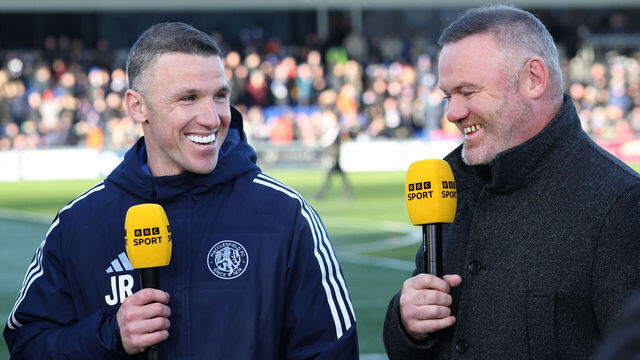Macclesfield Town manager John Rooney (L) is interviewed by his brother, former England star Wayne Rooney (R), before the start of the English FA Cup third round football match between Macclesfield Town and Crystal Palace at Leasing.com Stadium, Moss Rose in Macclesfield, northern England on January 10, 2026. / RESTRICTED TO EDITORIAL USE. No use with unauthorized audio, video, data, fixture lists, club/league logos or 'live' services. Online in-match use limited to 120 images. An additional 40 images may be used in extra time. No video emulation. Social media in-match use limited to 120 images. An additional 40 images may be used in extra time. No use in betting publications, games or single club/league/player publications. /