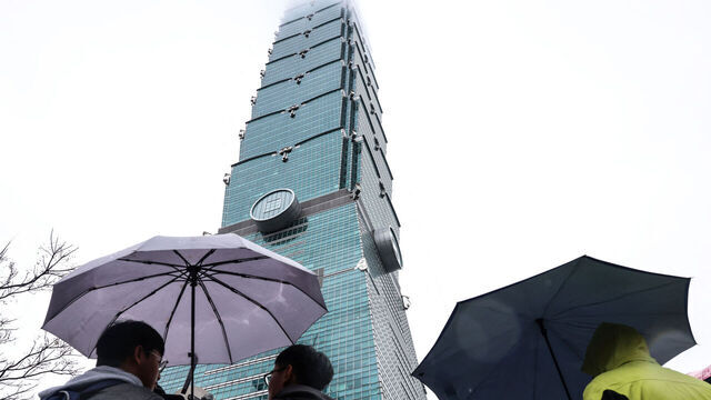 People hold umbrellas under the landmark Taipei 101 building, which US climber Alex Honnold was scheduled to scale but postponed due to bad weather, in Taipei on January 24, 2026.