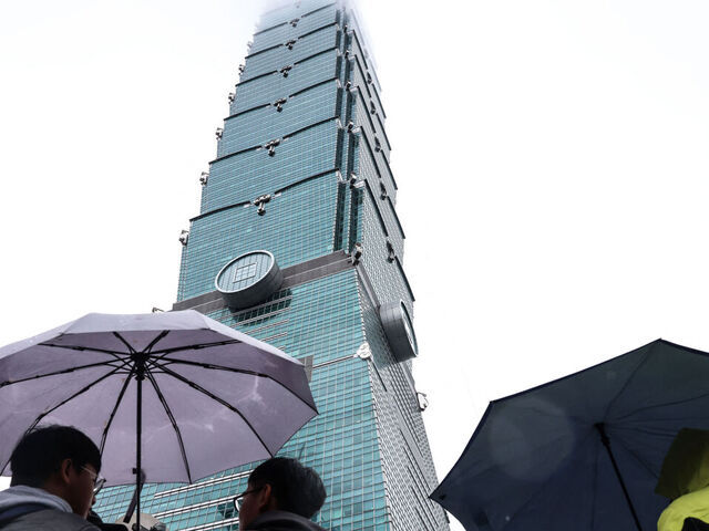 People hold umbrellas under the landmark Taipei 101 building, which US climber Alex Honnold was scheduled to scale but postponed due to bad weather, in Taipei on January 24, 2026.