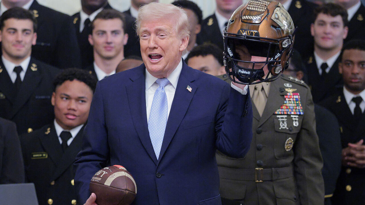 WASHINGTON, DC - MARCH 20: U.S. President Donald Trump holds up a helmet and football that were gifted to him during a ceremony awarding the Commander-in-Chief Trophy to the Navy Midshipmen football team in the East Room of the White House March 20, 2026 in Washington, DC. The Commander-in-Chief Trophy is awarded each year to the winner of the Army-Navy football game.