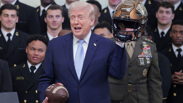 WASHINGTON, DC - MARCH 20: U.S. President Donald Trump holds up a helmet and football that were gifted to him during a ceremony awarding the Commander-in-Chief Trophy to the Navy Midshipmen football team in the East Room of the White House March 20, 2026 in Washington, DC. The Commander-in-Chief Trophy is awarded each year to the winner of the Army-Navy football game.