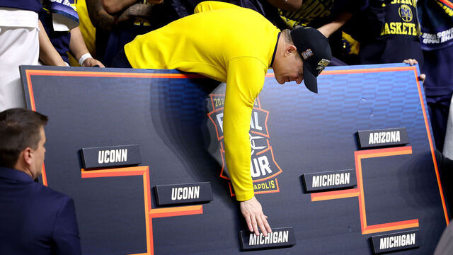 INDIANAPOLIS, INDIANA - APRIL 06: Head coach Dusty May of the Michigan Wolverines places the Michigan name on the championship bracket after defeating the UConn Huskies 69-63 in the National Championship of the 2026 NCAA Men's Basketball Tournament at Lucas Oil Stadium on April 06, 2026 in Indianapolis, Indiana.