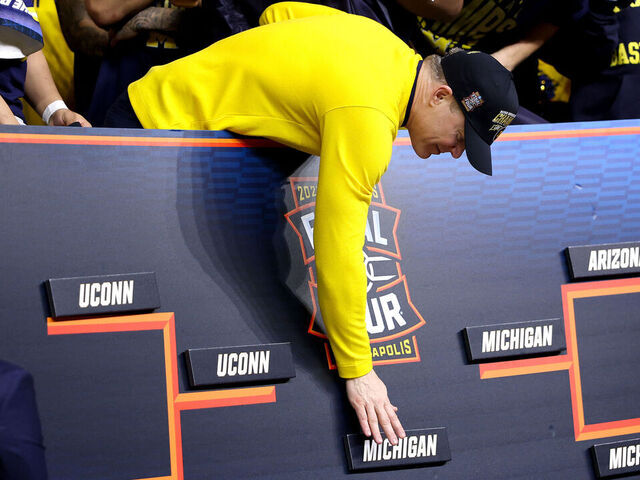 INDIANAPOLIS, INDIANA - APRIL 06: Head coach Dusty May of the Michigan Wolverines places the Michigan name on the championship bracket after defeating the UConn Huskies 69-63 in the National Championship of the 2026 NCAA Men's Basketball Tournament at Lucas Oil Stadium on April 06, 2026 in Indianapolis, Indiana.