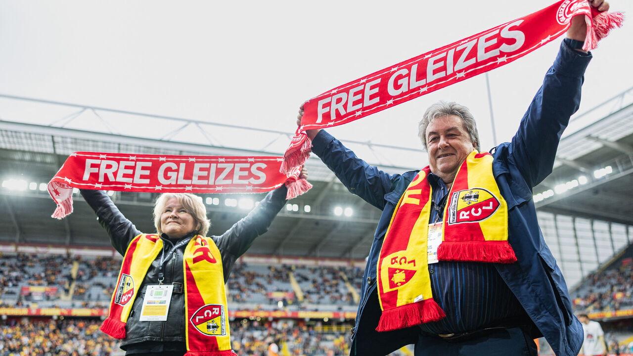 Sylvie Godard (R) and Francis Godard (L), mother and stepfather of jailed French sports journalist Christophe Gleizes, hold scarfs calling of the release of their son ahead of the friendly football match between RC Lens and FC Rouen in solidarity with Christophe Gleizes at the Stade Bollaert-Delelis in Lens, northern France, on April 11, 2026. Gleizes was arrested in May 2024 and sentenced to seven years in prison in Algeria while travelling to northeastern Algeria's Kabylia region to write about the country's most decorated football club, Jeunesse Sportive de Kabylie.
