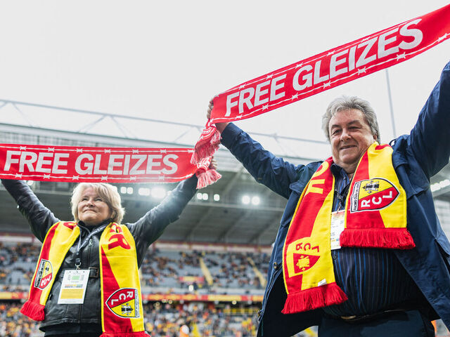 Sylvie Godard (R) and Francis Godard (L), mother and stepfather of jailed French sports journalist Christophe Gleizes, hold scarfs calling of the release of their son ahead of the friendly football match between RC Lens and FC Rouen in solidarity with Christophe Gleizes at the Stade Bollaert-Delelis in Lens, northern France, on April 11, 2026. Gleizes was arrested in May 2024 and sentenced to seven years in prison in Algeria while travelling to northeastern Algeria's Kabylia region to write about the country's most decorated football club, Jeunesse Sportive de Kabylie.