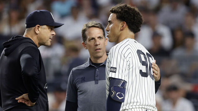 NEW YORK, NEW YORK - AUGUST 29: George Lombard Jr. #96 of the New York Yankees (R) is checked on by manager Aaron Boone #17 (L) and trainer Tim Lentych (C) after a swing during his second inning at-bat against the Boston Red Sox in game two of the doubleheader at Yankee Stadium on August 29, 2026 in New York City. Lombard Jr. later left the game.