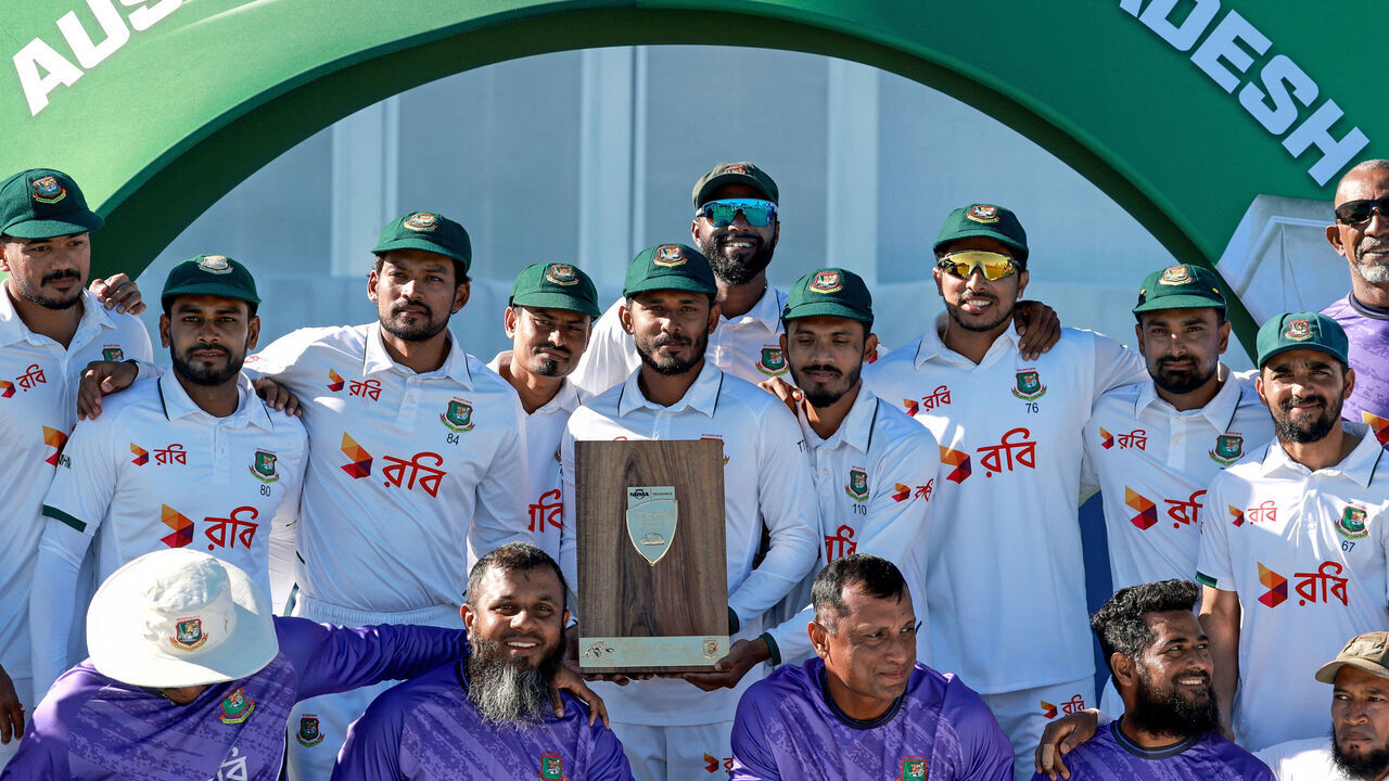 Bangladesh's captain Najmul Hossain Shanto (C) holds the series trophy as he poses with team mates and team officials after the second day of the second cricket Test match between Australia and Bangladesh at the Great Barrier Reef Stadium in Mackay on August 23, 2026. / -- IMAGE RESTRICTED TO EDITORIAL USE - STRICTLY NO COMMERCIAL USE --