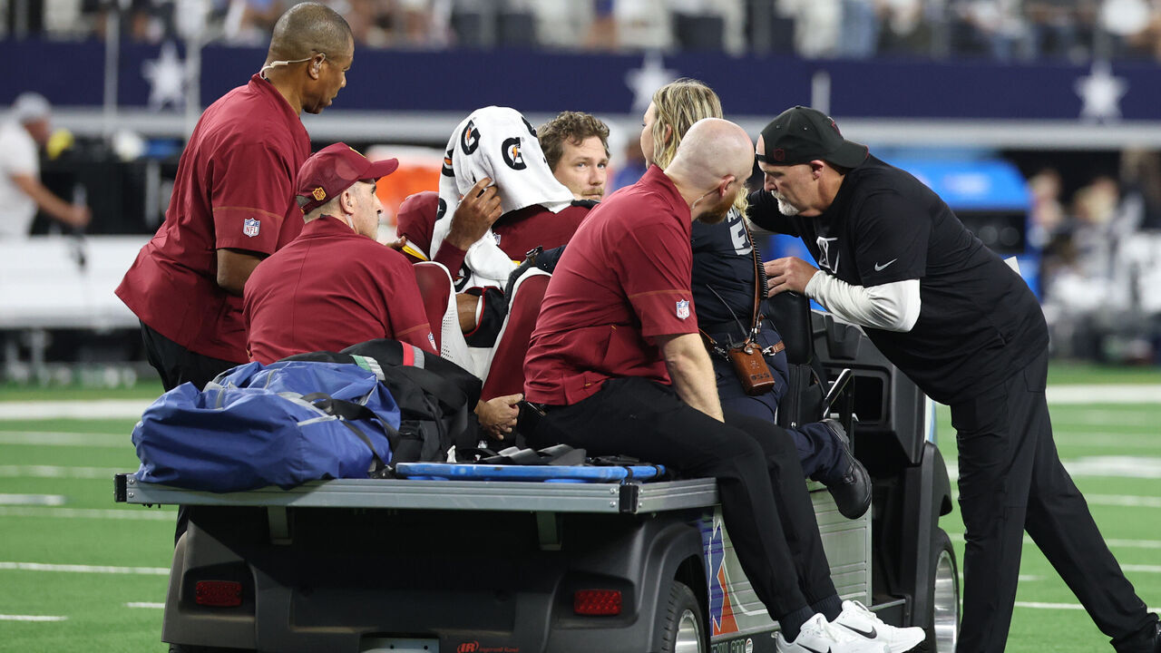 ARLINGTON, TEXAS - SEPTEMBER 20: Head coach Dan Quinn of the Washington Commanders talks to Jayden Daniels #5 of the Washington Commanders as Daniels is carted off the field in the second quarter of a game against the Dallas Cowboys at AT&T Stadium on September 20, 2026 in Arlington, Texas.
