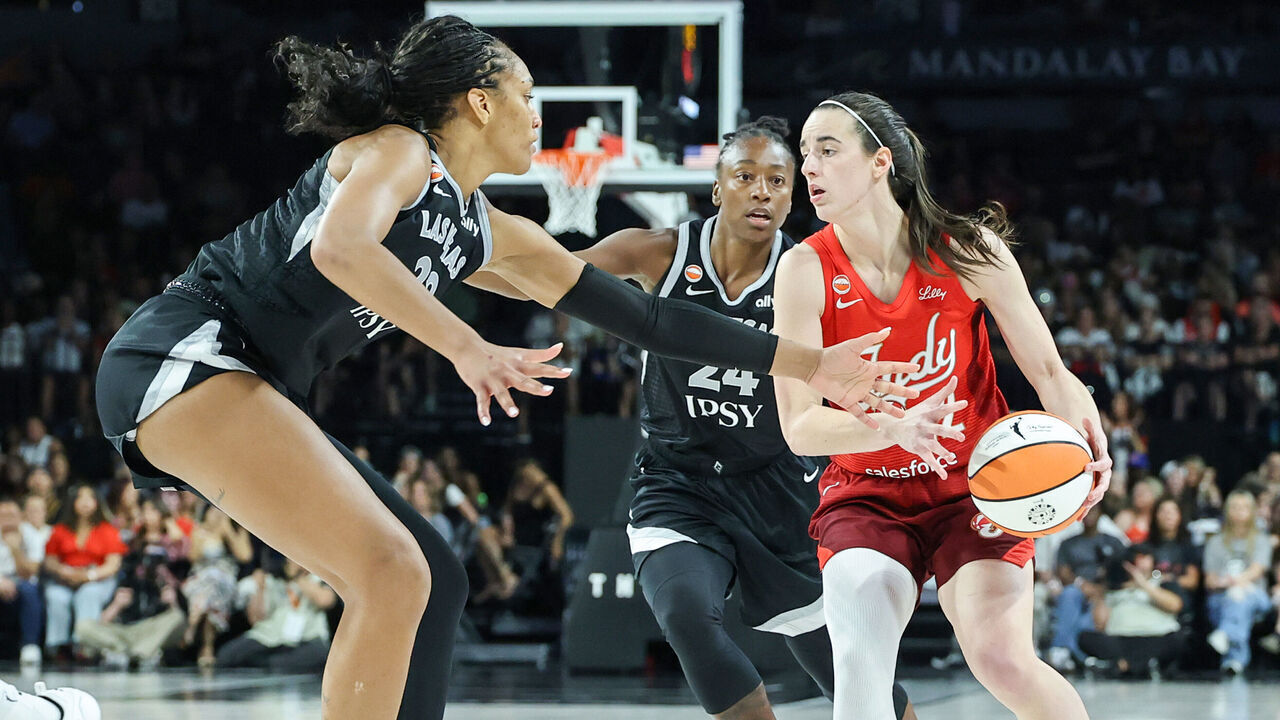LAS VEGAS, NEVADA - JULY 12: Caitlin Clark #22 of the Indiana Fever drives against A'ja Wilson #22 and Jewell Loyd #24 of the Las Vegas Aces in the fourth quarter of their game at Michelob ULTRA Arena on July 12, 2026 in Las Vegas, Nevada. The Fever defeated the Aces 109-75.
