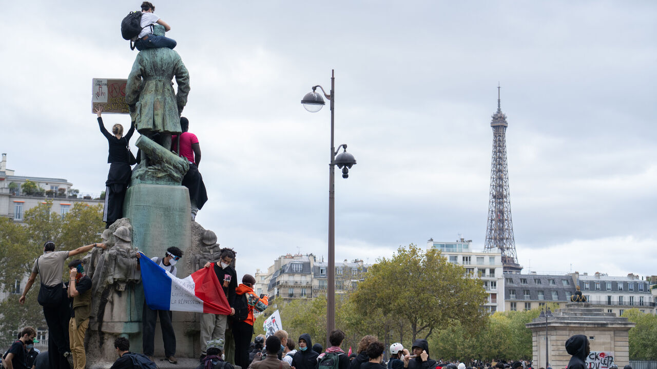 PARIS, FRANCE - OCTOBER 13: Protestors climb on the Statue of Marie Emile Fayolle on Place Vauban facing the Eiffel Tower, on October 13, 2026 in Paris, France. The French high school protests and riots have entered a new phase this week as student and teacher unions mobilise for a massive nationwide day of action aimed at forcing systemic changes after rejecting the government's emergency offer of 3,000 substitute teachers. Driven by deep-seated fury over severe underfunding, critical staff shortages, and crumbling, unventilated classrooms exposed by extreme summer heatwaves, the movement has shut down hundreds of campuses and frequently erupted into violent clashes between youth and riot police.