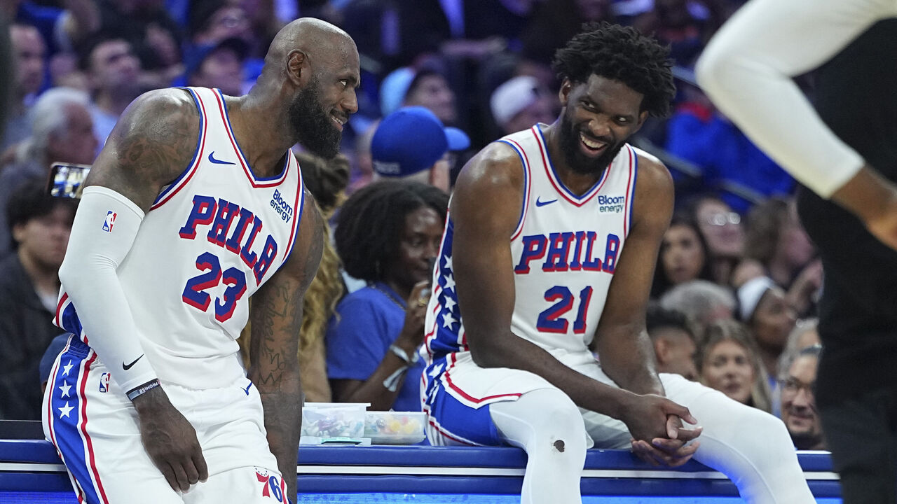 PHILADELPHIA, PENNSYLVANIA - OCTOBER 16: LeBron James #23 and Joel Embiid #21 of the Philadelphia 76ers laugh during a timeout against the Boston Celtics during the preseason game at Xfinity Mobile Arena on October 16, 2026 in Philadelphia, Pennsylvania.