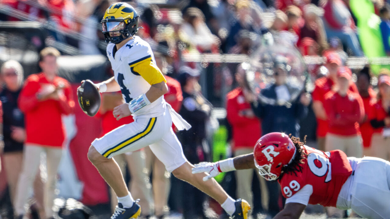 PISCATAWAY, NEW JERSEY - OCTOBER 31: Quarterback Tommy Carr #14 of the Michigan Wolverines avoids a tackle by Defensive lineman Rondo Porter #99 of the Rutgers Scarlet Knights during the second quarter at SHI Stadium on October 31, 2026 in Piscataway, New Jersey.